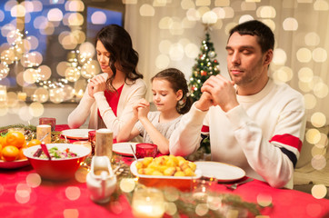 holidays, family and celebration concept - happy mother, father and little daughter having christmas dinner and praying before meal at home
