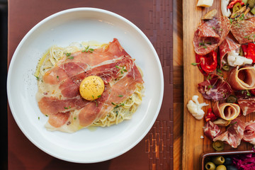 Top view of Fettuccine Carbonara with parma ham and yolk with black pepper. Served in white plate with Cold Cuts.
