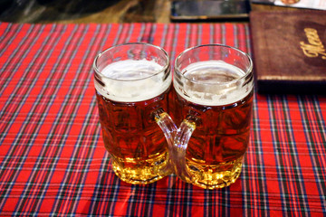 two mugs fresh beer on checkered tablecloth, symbolizing Oktoberfest.