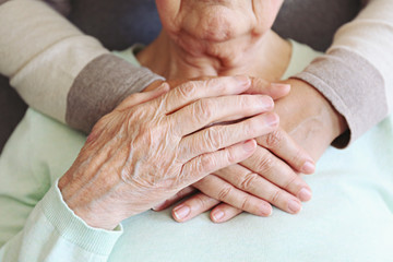 Mature female in elderly care facility gets help from hospital personnel nurse. Senior woman w/ aged wrinkled skin & care giver, hands close up. Grand mother everyday life. Background, copy space.