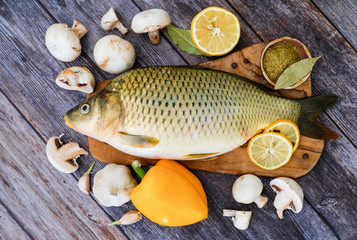 Fresh fish ready to cook. Carp on a wooden kitchen Board in the kitchen surrounded by vegetables (pepper, garlic, cherry tomatoes, lemon). 