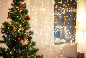 winter holidays and interior concept - close up of decorated christmas tree, sofa and garland on window at home in evening