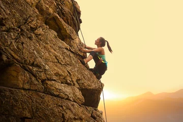 Fotobehang Beautiful Woman Climbing on the Rock at Foggy Sunset in the Mountains. Adventure and Extreme Sport Concept © Maksym Protsenko