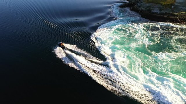 Aerial, drone top view shot as a man on a jet ski trying to climb on a river at a giant vortex. Saltstraumen tidal current in Norway.