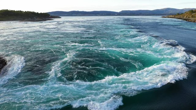 Low flying aerial drone shot over the Saltstraumen tidal current as breaking up, forming a huge vortex over on the water, as sea birds flying by. Waves splashing white foam on the top.