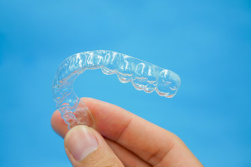 hand holding clear plastic retainer teeth that isolated on blue sky background. it's an equipment for orthodontist give the patient to orthodontic surgery in dental clinic or hospital