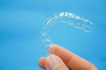 hand holding clear plastic retainer teeth that isolated on blue sky background. it's an equipment for orthodontist give the patient to orthodontic surgery in dental clinic or hospital - obrazy, fototapety, plakaty