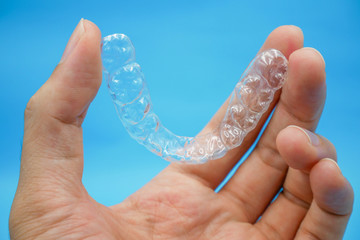 hand holding clear plastic retainer teeth that isolated on blue sky background. it's an equipment for orthodontist give the patient to orthodontic surgery in dental clinic or hospital