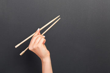 Creative image of wooden chopsticks in female hand on black background. Japanese and chinese food...