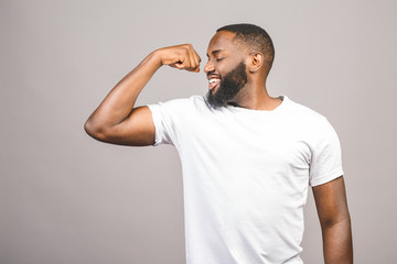 Close up portrait of a happy young african american man flexing bicep muscle isolated against grey background.