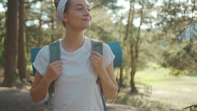 Attractive young woman tourist with backpack walking in the fall forest on sunny summer day smile look around vacation camping hiking travel wood freedom journey young nature activity slow motion
