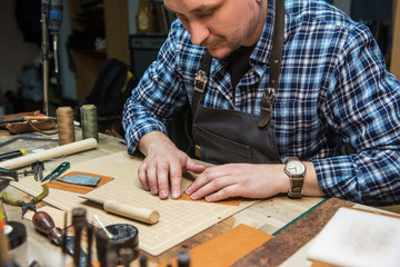 Man working with leather textile at a workshop. Craftman cutting leather. Concept of handmade craft production of leather goods.