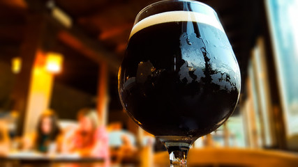 Glass of fresh dark beer on rustic pub background