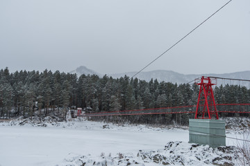 Suspension hanging bridge above winter frozen mountain Katun river, Altai mountains, Siberia, Russia