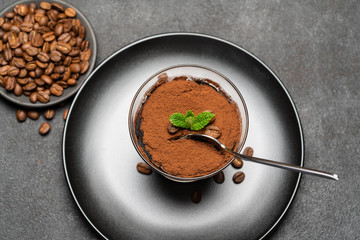 Portion of Classic tiramisu dessert in a glass cup on dark concrete background