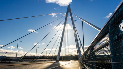 Northern Spire Bridge (opened Summer 2018) in Sunderland spanning the River Wear.  Photo taken facing the sun giving the bridge a silhouette contrasting with the blue sky with dark and white clouds. - obrazy, fototapety, plakaty