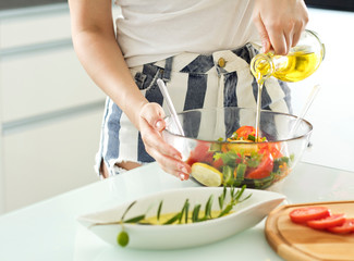 healthy eating, vegetarian food, dieting and people concept - close up of young woman dressing vegetable salad with olive oil at home