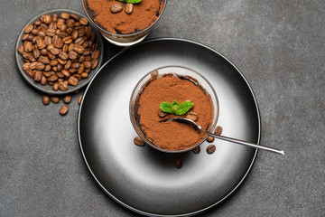 Portion of Classic tiramisu dessert in a glass cup on dark concrete background