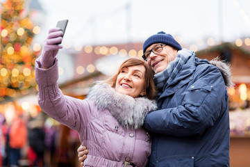 technology, winter holidays and people concept - happy senior couple taking selfie by smartphone at...