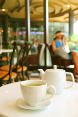 Vertical image of a white cup and teapot of green tea served on cafe's white table