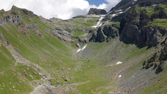 4K Aerial Drone View of Stream flows out of Mountain revealing white clouds in Valle del Lys. Drone tilt up