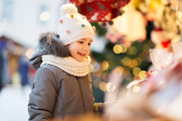 holidays, childhood and people concept - happy little girl at christmas market in winter