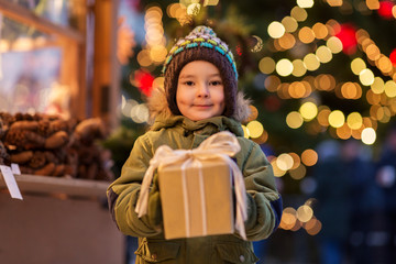 Fototapeta na wymiar holidays, childhood and people concept - happy little boy with gift box at christmas market in winter evening