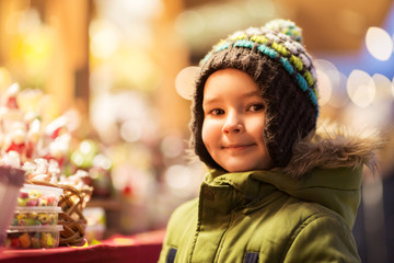 holidays, childhood and people concept - happy little boy at christmas market candy shop in winter...
