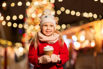 holidays, childhood and people concept - happy little girl with cup of tea at christmas market in...