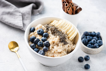 Oatmeal porridge with fruits, berries and chia seeds in white bowl. Concept of healthy breakfast food, clean eating, weight loss - obrazy, fototapety, plakaty
