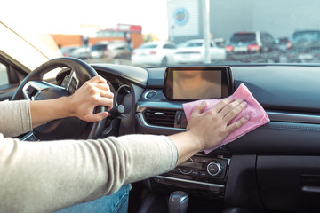 Close-up, hand wipes dust with pink cloth, inside car, clean and care for inside of the car, in the summer in the city in the parking lot at the store, in free time from driving a car.