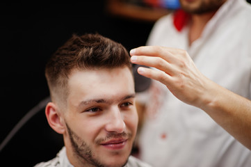 Young bearded man getting haircut by hairdresser while sitting in chair at barbershop. Barber soul.