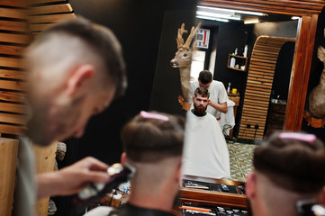 Young bearded man getting haircut by hairdresser while sitting in chair at barbershop. Barber soul.