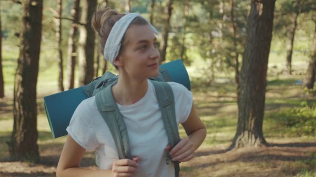 Slow motion woman tourist with backpack walking in the fall forest on sunny summer day smile look around vacation camping hiking travel wood hike active journey young nature people activity close up