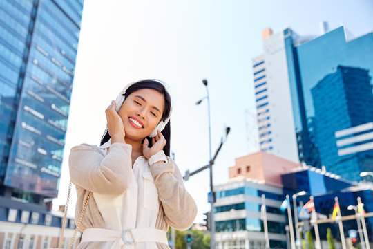 technology, leisure and people concept - happy smiling asian woman with headphones listening to music in city