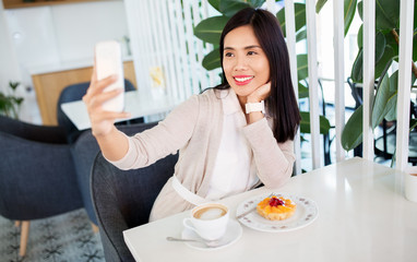 technology and people concept - happy asian woman with cake and coffee taking selfie by smartphone at cafe
