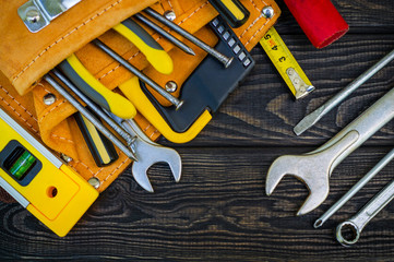 Tools in the bag for carpentry and accessories on a wooden black vintage background.