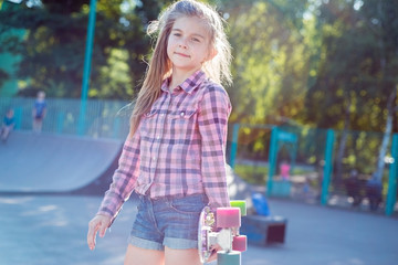 portrait of a beautiful little teenage girl, holding a skateboard, against the backdrop of a...