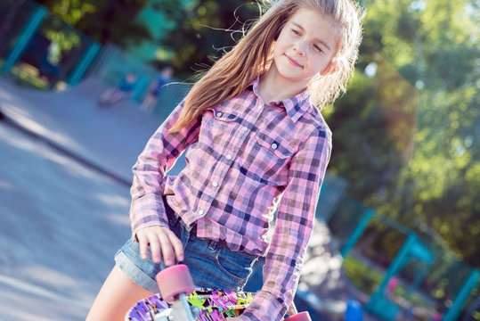 portrait of a beautiful little girl, holding skateboard on skatepark, active lifestyle of children, in an unusual perspective