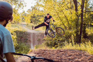 cyclist - a friend looks like young guy does jumps and bike stunts. in the forest against the setting sun