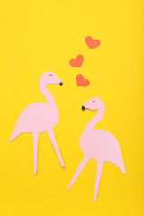 Pink paper flamingos and red hearts on yellow background. Minimalism concept