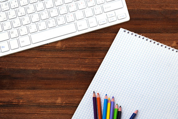 Modern aluminum computer keyboard, empty notebook and colorful pencil on wooden background