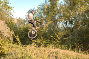 Fototapeta na wymiar young guy cyclist jumping high and doing tricks with a bicycle. unusual angle. in the forest against sunset
