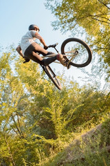 young guy cyclist jumping high and doing tricks with a bicycle. unusual angle. in the forest...