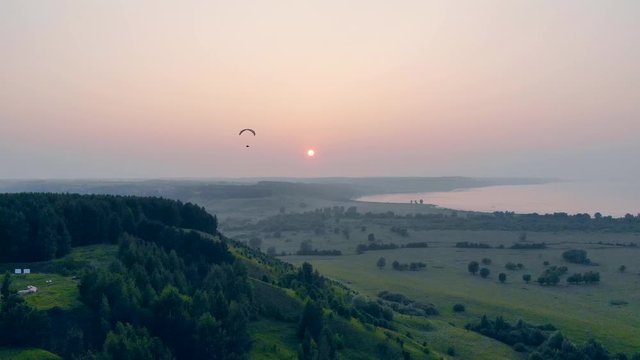 One man floats above green field on a glider.