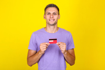 Young man holding credit card on yellow background