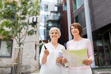 tourism, travel and friendship concept - happy senior women with map and city guide taking picture by smartphone on selfie stick on street in tallinn
