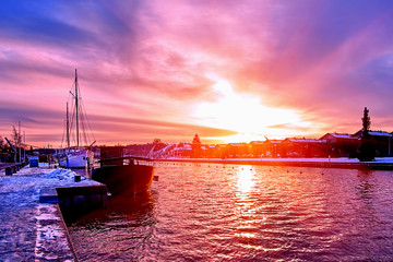 Scenic red purple and violet sunset over countryside river in Europe with old ships having rest at the snowy harbor pier - 287441829