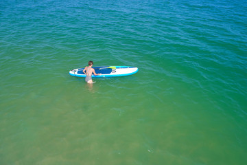 Aerial drone birds eye view of young woman exercising sup board in turquoise tropical clear waters