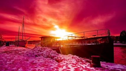 Scenic red purple and violet sunset over countryside river in Europe with old ships having rest at the snowy harbor pier - 287441852